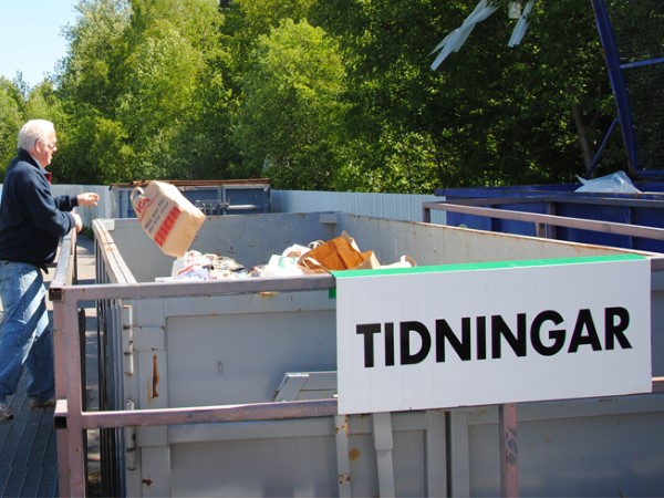 En person som kastar tidningar för sortering på återvinningscentral